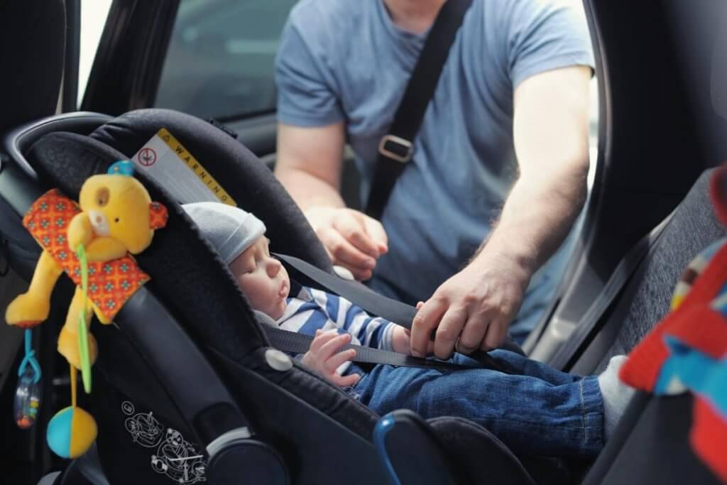 a man strapping a small infant asleep into the back of a car
