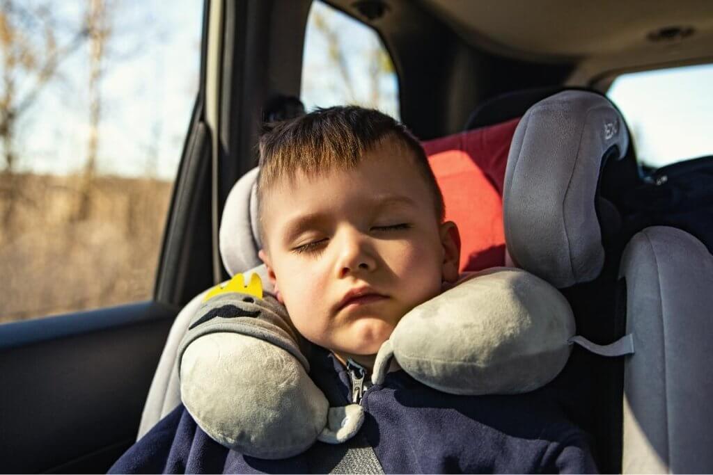 A small child in a car seat asleep with a toddler neck pillow
