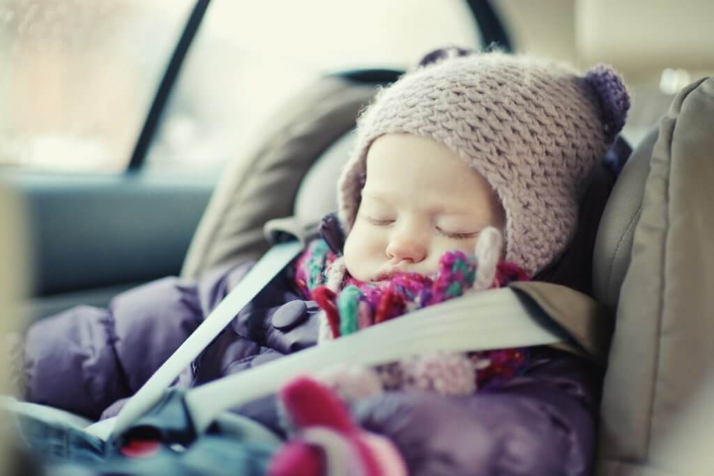 A baby in a car seat wrapped in warm jacket and beanie