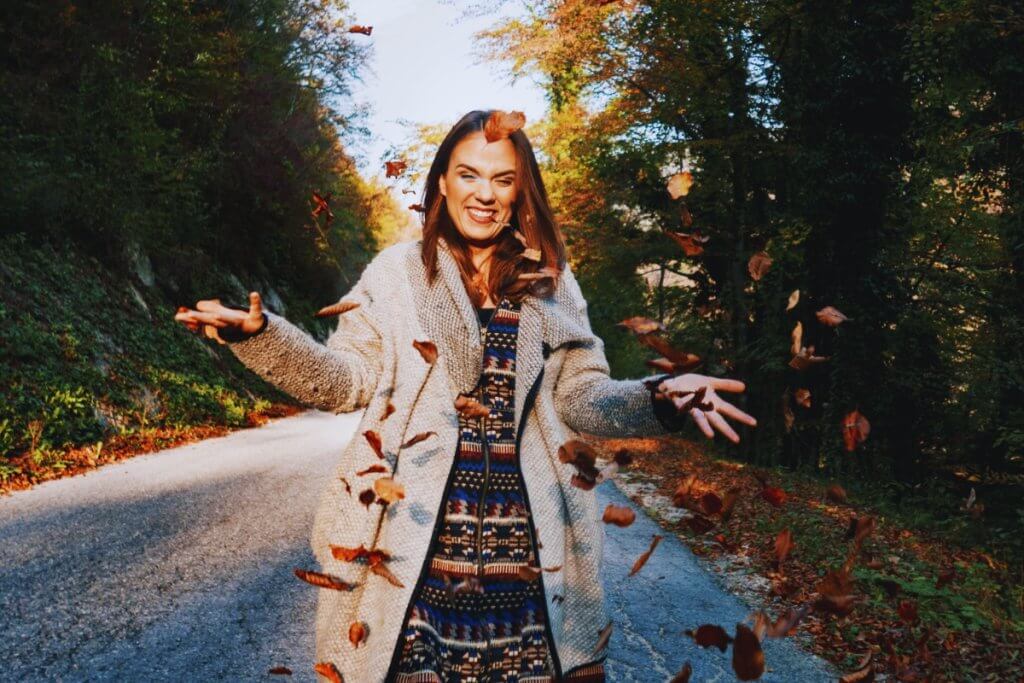 Outfits for fall lasy in the road throwing fall leaves wearing a long beige overcoat