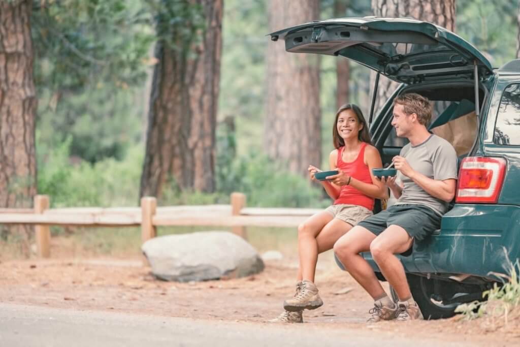 couple eating a meal in the back of their SUV car in thr forest, road trip meal guide